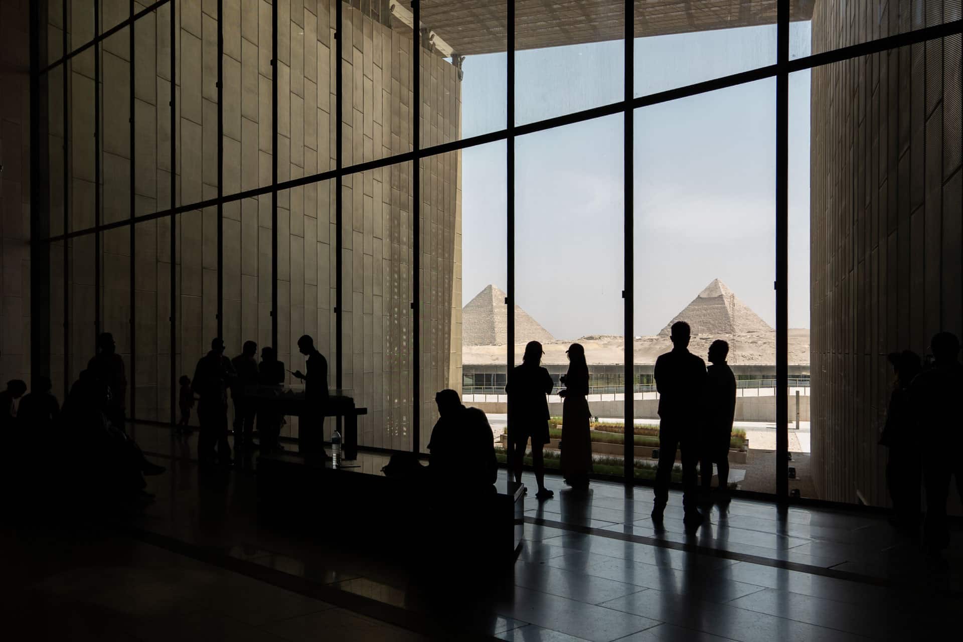 Reisende vor dem Panoramafenster im Grand Egyptian Museum mit Blick auf die Pyramiden von Gizeh, Ägypten, Globetrotter Select