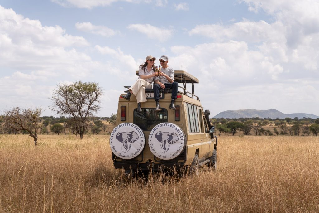 Select-Zelt-Safari Reisende auf Safarifahrzeug stoßen mit Bier an, Tansania, Globetrotter Select