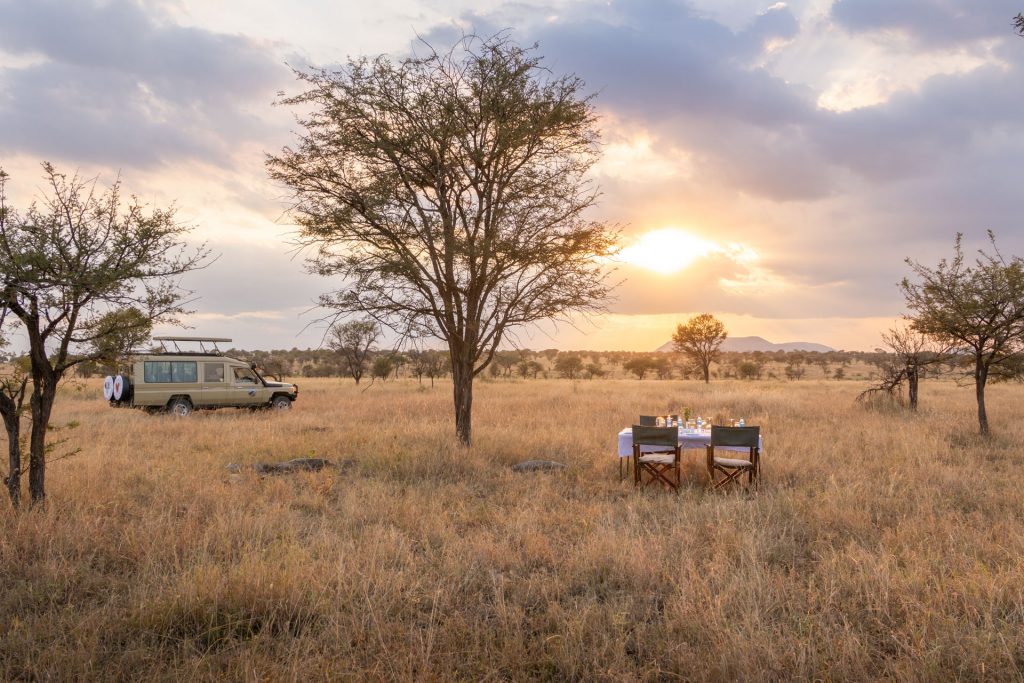 Tansania Zeltsafari – Ihr privates Camp in der Serengeti Safarifahrzeug und gedeckter Tisch in der Savanne bei Sonnenuntergang, Select-Zelt-Safari, Serengeti Tansania, Globetrotter Select
