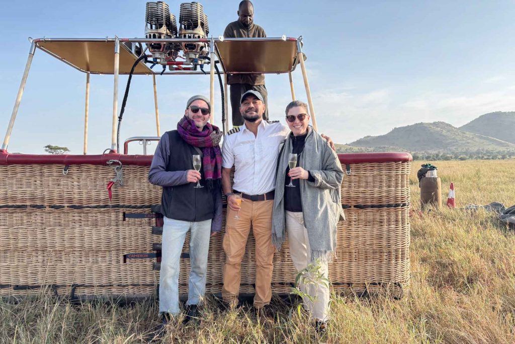 Team-Mitglieder von Globetrotter Select mit Piloten vor Heißluftballon in der Serengeti, Tansania